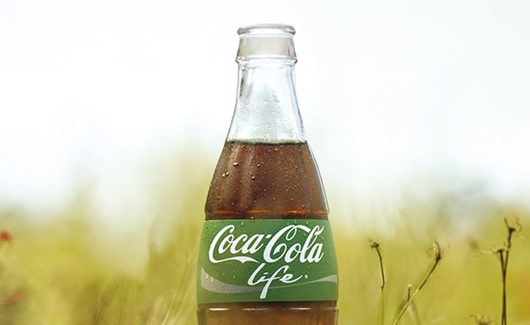 An image of a crisp Coca-Cola Life bottle sitting outside in the grass.
